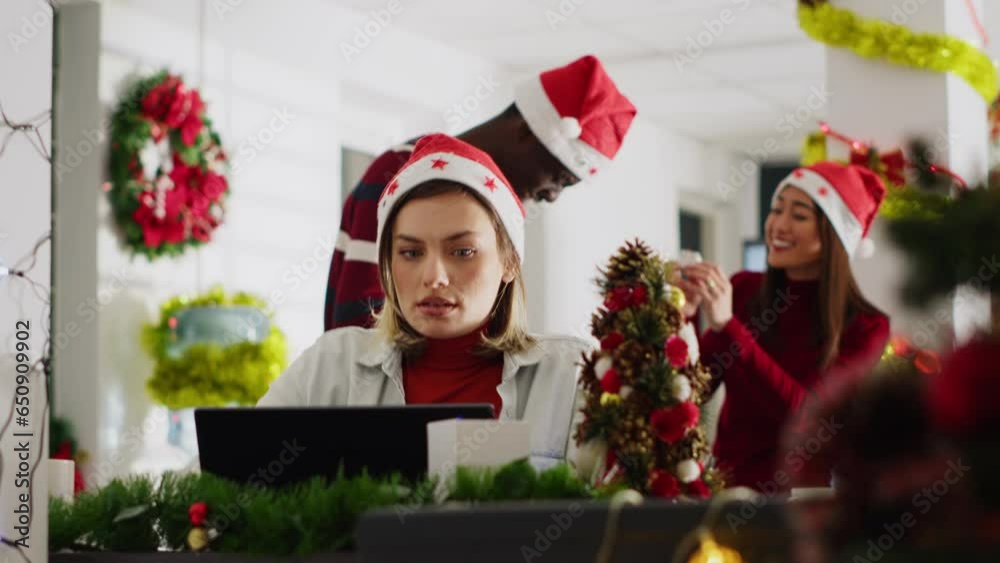 Woman filling paperwork in Christmas decorated office, perturbed by disturbing staff members discussing in background. Employee unable to concentrate on tasks while colleagues talk loudly Woman filling paperwork in Christmas decorated office, perturbed by disturbing staff members discussing in background. Employee unable to concentrate on tasks while colleagues talk loudly