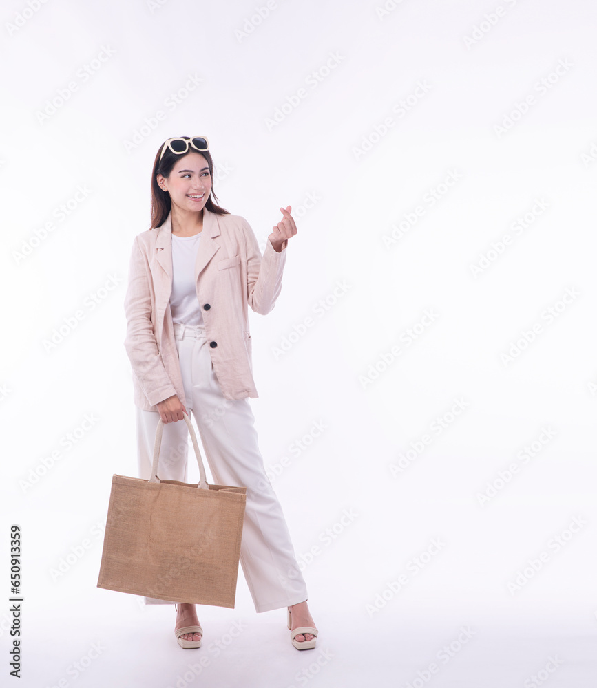 Excited cheerful asian woman wear suit carry eco tote handbag using finger making mini heart standing on isolated white background. Shopper girl looking at camera for shopping online advertisement.