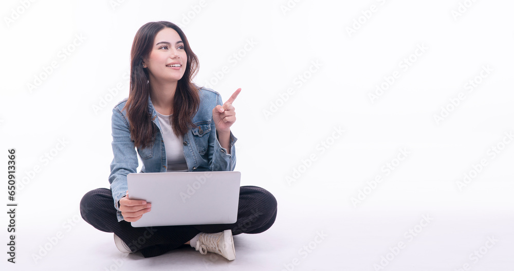 Cheerful asian woman using laptop pointing finger looking empty copy space sitting on floor over isolated white background. Positive student teenager use finger pointing present product with computer. Cheerful asian woman using laptop pointing finger looking empty copy space sitting on floor over isolated white background. Positive student teenager use finger pointing present product with computer.