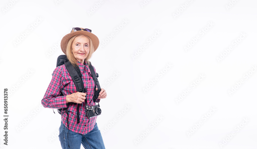 Healthy active cool elderly woman casual jeans with backpack hat standing over isolated white background. Cheerful retired female sunglasses on hat hold camera carefree vacation adventure holiday. Healthy active cool elderly woman casual jeans with backpack hat standing over isolated white background. Cheerful retired female sunglasses on hat hold camera carefree vacation adventure holiday.
