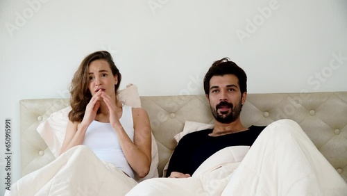Excited couple cheering football game in tv sitting together at bedroom. Young man watching tv championship match soccer with wife in blanket raised hands excitement shock win at home. photo