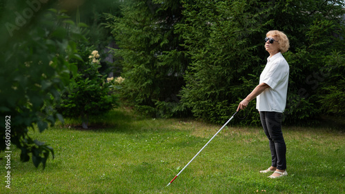 Elderly blind woman walking in the park with a tactile cane. 