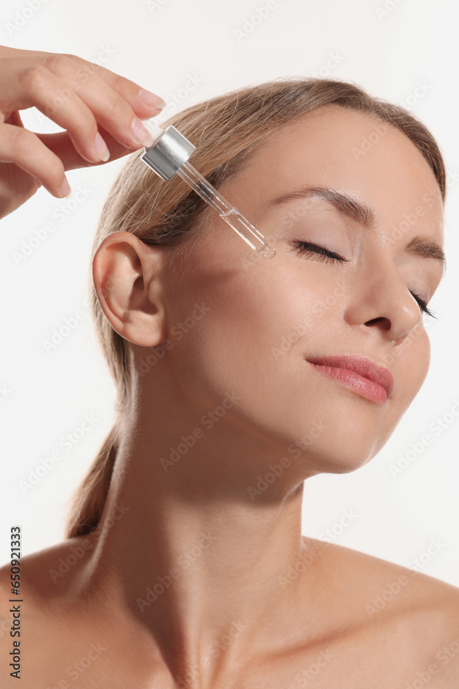 Beautiful woman applying cosmetic serum onto her face on white background