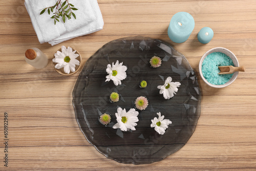 Plate with water, flowers, burning candles and sea salt on wooden floor, flat lay. Pedicure procedure