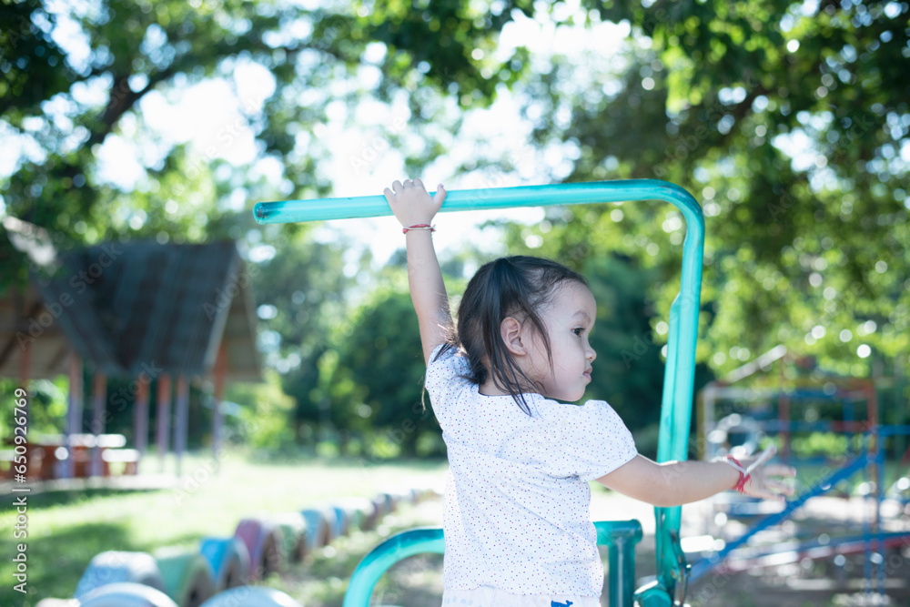 Obraz premium Asian girl playing on the playground with a trapeze Enthusiastic child hanging on the bar with two hands Children exercising.