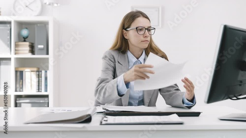 Busy businesswoman typing on computer in office, sighing deeply and frowning, annoyingly looking for information in documents photo