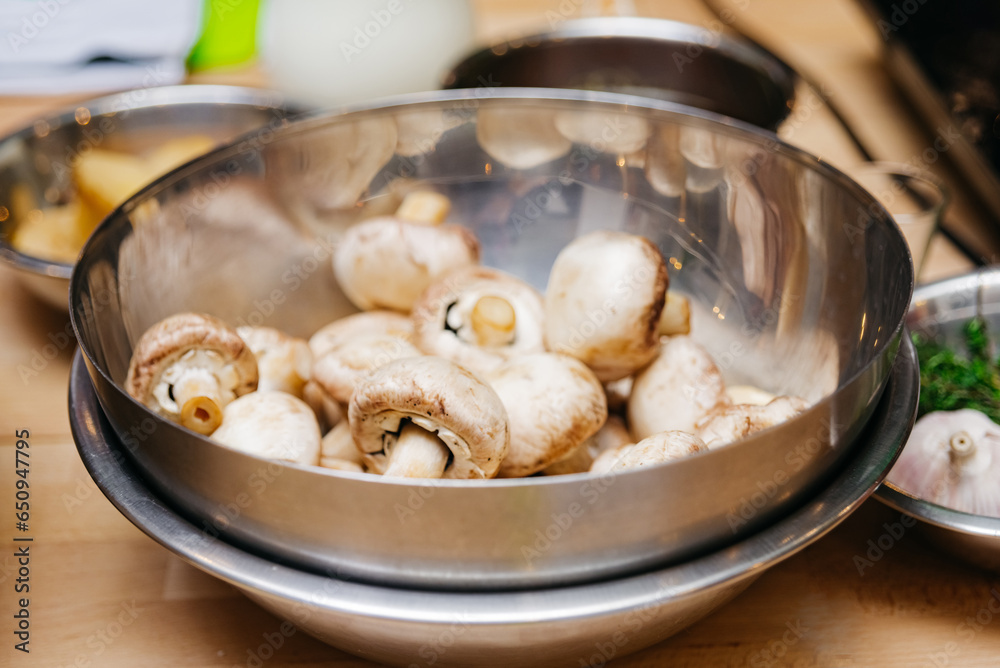Fresh champignon mushrooms in a metal bowl on a wooden table, raw food ready to cook Fresh champignon mushrooms in a metal bowl on a wooden table, raw food ready to cook