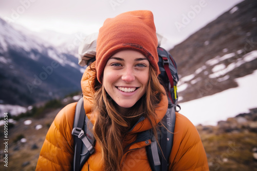 Young woman smiling in jacket and backpack hiking up snowy mountain