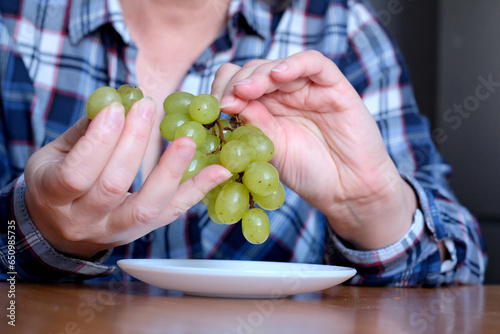 The hands of an elderly woman holds a small brush of white seedless grapes
