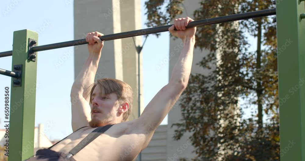 Young man performs impressive tricks on horizontal bar in an urban workout area. Shirtless male portrait showcases a sporty, healthy physique, reflecting dedication to physical fitness. Strong body Young man performs impressive tricks on horizontal bar in an urban workout area. Shirtless male portrait showcases a sporty, healthy physique, reflecting dedication to physical fitness. Strong body