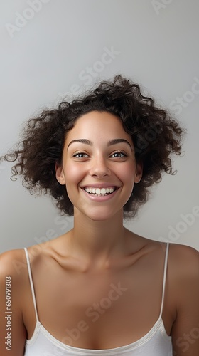 Image of smiling confident young woman in white T-shirt looking at camera isolated in grey background