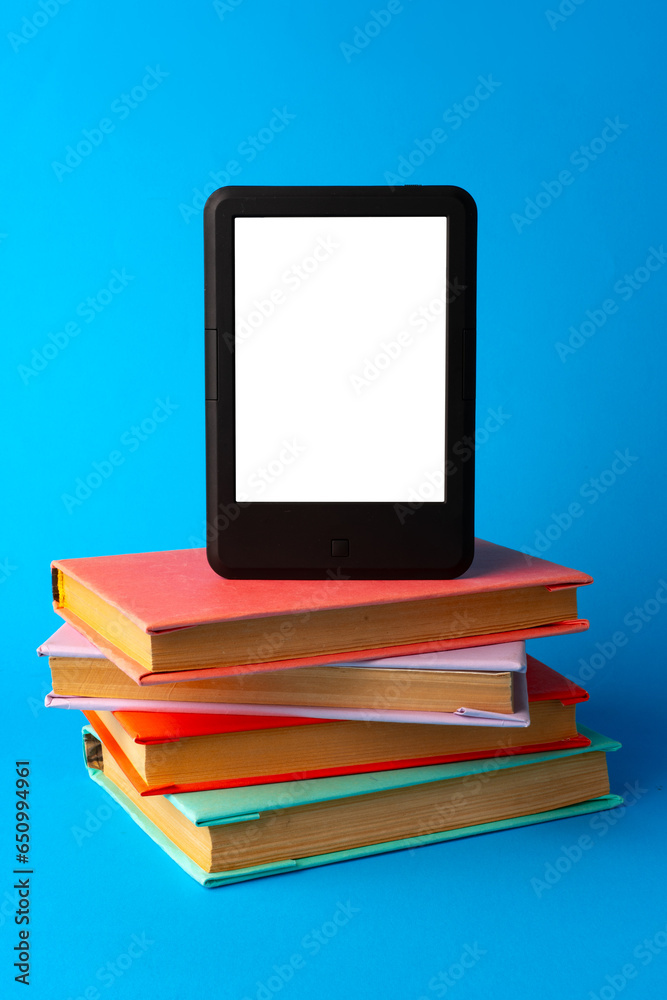 Modern e-book on stack of hardcover books on blue background Modern e-book on stack of hardcover books on blue background