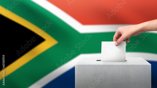 Woman puts ballot paper in voting box on South Africa flag background. Election concept.