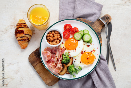 Traditional Englis breakfast plate with bacon strips, sunny side up eggs, vegetables and cake on light background photo