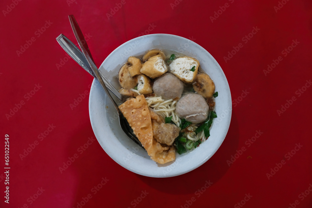 A bowl of soup containing noodles, meatballs, fried tofu and dumplings