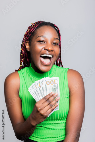 Happy smiley delighted African American dark skinned woman with braids smiling celebrating receiving her first salary holding bunch of money banknotes cash concept wasting spending money. photo