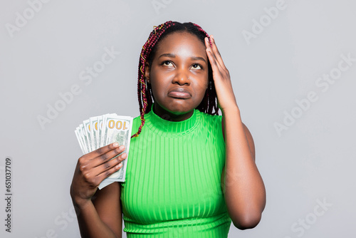 Tired dissatisfied African American dark skinned woman with colourful braids tired fed up with evrything bills loans debts holding bunch of money dollars in hands counting low sallary. photo