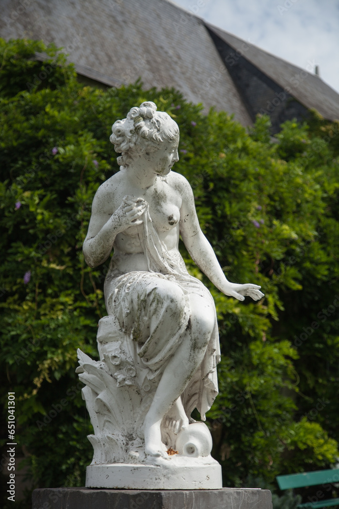 Statue de femme en pierre blanche contre un fond de feuillage
