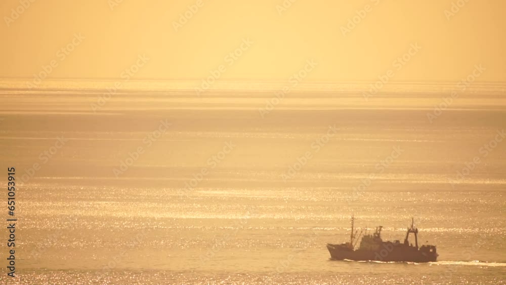 Fishing ship trawler at sunset in the sea. Abstract aerial sea summer ocean sunset nature background. Small waves on calm water surface in motion blur with golden bokeh lights from sun. Fishing ship trawler at sunset in the sea. Abstract aerial sea summer ocean sunset nature background. Small waves on calm water surface in motion blur with golden bokeh lights from sun.