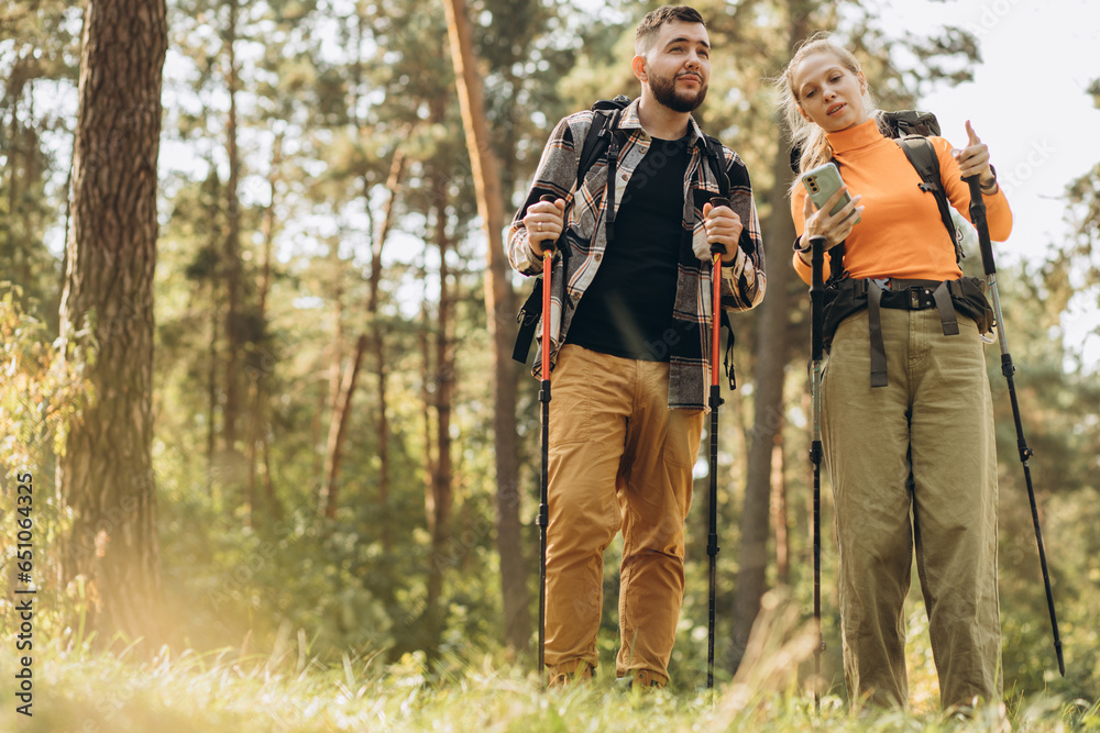 Couple hiking with bags and walking sticks in forest