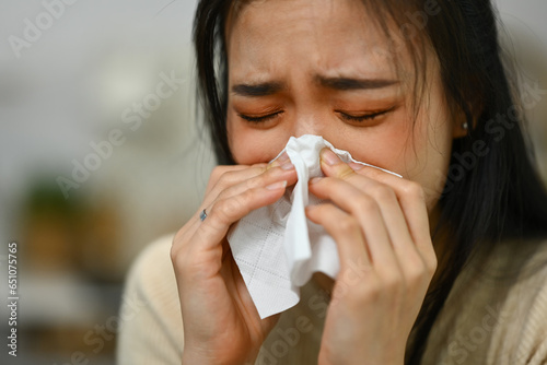 Sick woman having allergy symptoms ,blowing nose and sneezing in tissue. People and health problems
