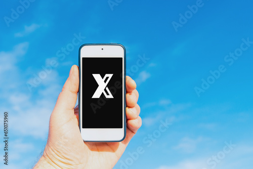 Person holding mobile phone with a letter X on the screen.Blue sky with cloud blurred background.