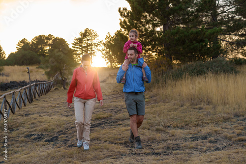 Sunset Stroll: Mediterranean family's full-figure silhouette on a mountain path, with a moody child sitting atop her father's shoulders.
