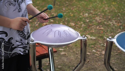 playing and creating music on a metal glucophone with the hands of a teenager with sticks, in a city park in autumn against the background of fallen leaves photo