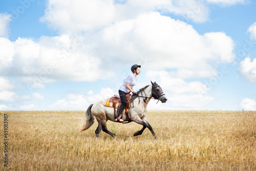 A young teenage girl gallops on a horse across a field, against the backdrop of a cloudy sky. Horse riding, horse riding, horse riding lessons.