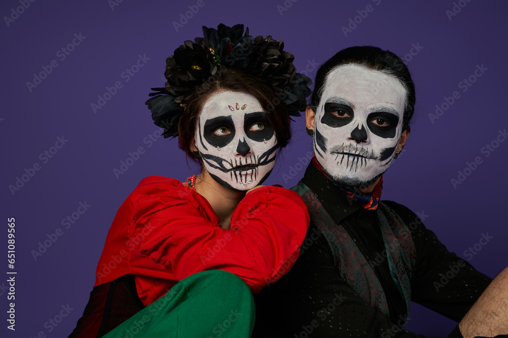 dia de los muertos couple, woman in catrina makeup and black wreath leaning on spooky man on blue