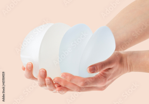  Female hands holding stack of different types of breast implants.