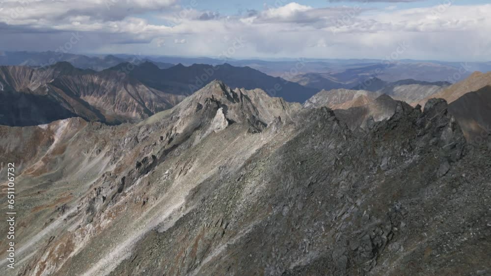 Flying over the picturesque bare rocks of the Eastern Sayan mountains. Beautiful peaks on the background of clouds. Epicness of wild nature Flying over the picturesque bare rocks of the Eastern Sayan mountains. Beautiful peaks on the background of clouds. Epicness of wild nature