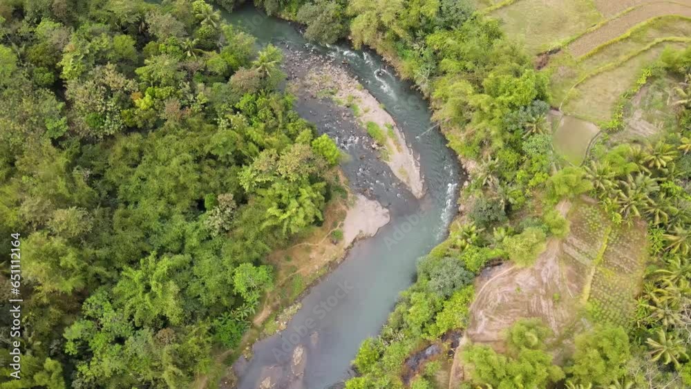Orbit drone shot of winding rocky river flows on tropical country with dense trees and plantation. Elo river in Indonesia. Filmed in 4k, drone video. Orbit drone shot of winding rocky river flows on tropical country with dense trees and plantation. Elo river in Indonesia. Filmed in 4k, drone video.