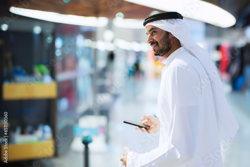 Full body of walking Arab man indoors. Emirati wearing Kandura inside a shopping mall or metro station or airport or hotel concept photo