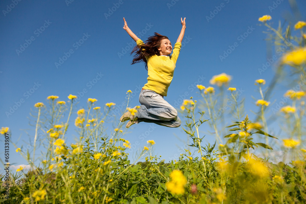 Happy and beautiful young woman in a bright yellow sweater and blue jeans jumping high in a sunny summer field. Happy and beautiful young woman in a bright yellow sweater and blue jeans jumping high in a sunny summer field.