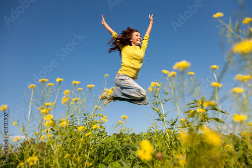 Happy and beautiful young woman in a bright yellow sweater and blue jeans  jumping high in a sunny summer field.