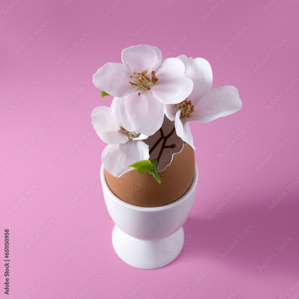 Small vase made of brown eggshell in white egg cup with apple blossoms. Easter concept. Square, pink background. Small vase made of brown eggshell in white egg cup with apple blossoms. Easter concept. Square, pink background.