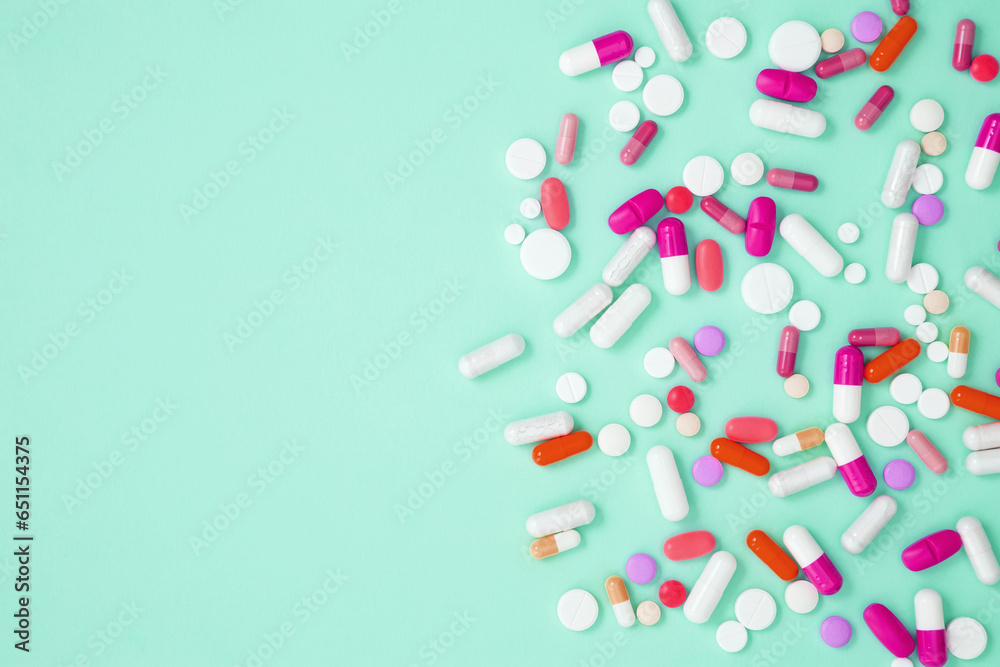 Various white medication tablets and capsules on green background. Concept of healthcare and medicine. Top view, copy space