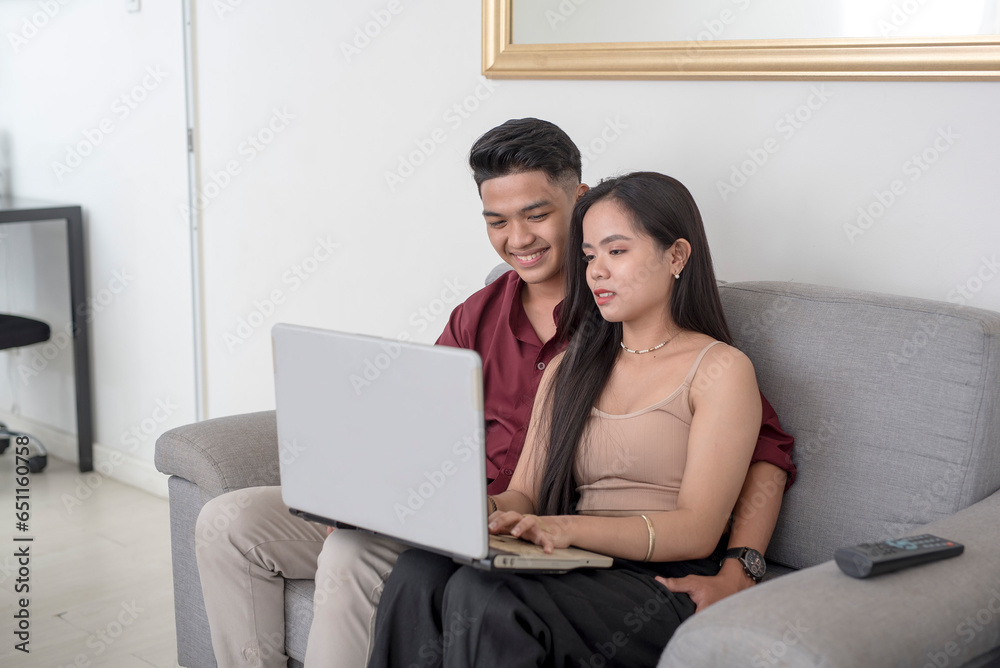A young professional typing on her laptop while hanging out with her boyfriend at the sofa. Candid scene at the living room.