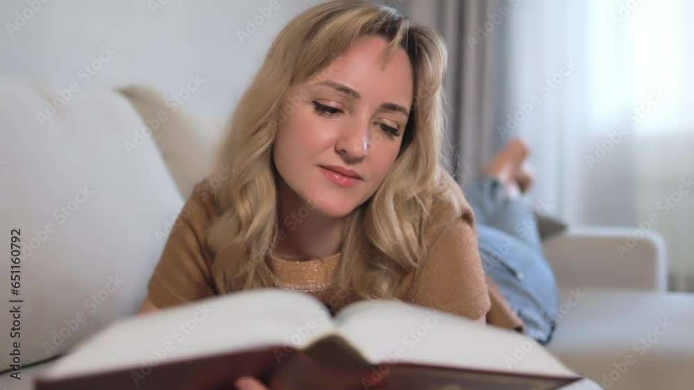 A blonde woman with curls on the sofa reads a book. A blonde woman with curls on the sofa reads a book.