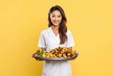Young Beautiful Asian Doctor Nutritionist Holding a Tray with Fresh Vegetables on yellow Background