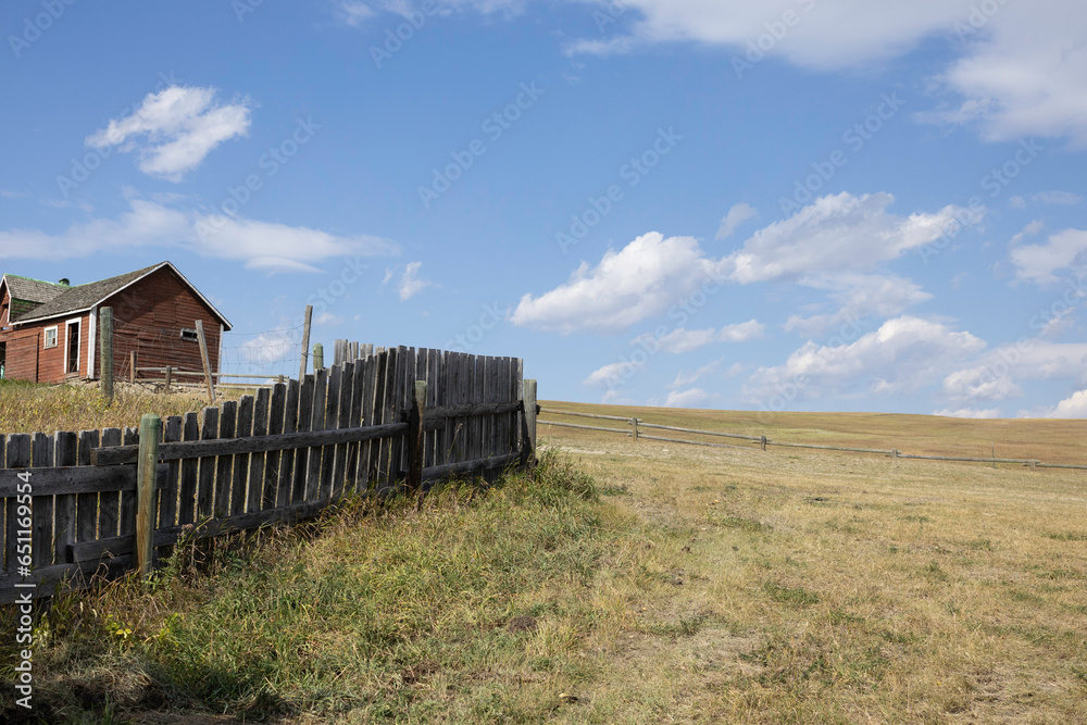 Rural scene on a cattle ranch of a weathered wooden fence leading to an old red shed and the open pasture behind them.