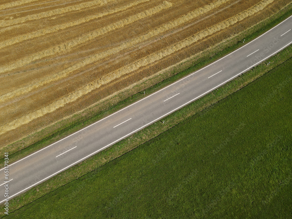 Aerial view of a road between a mowed hay field and a green grass field 