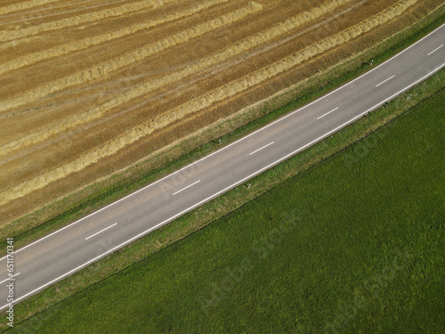 Aerial view of a road between a mowed hay field and a green grass field 