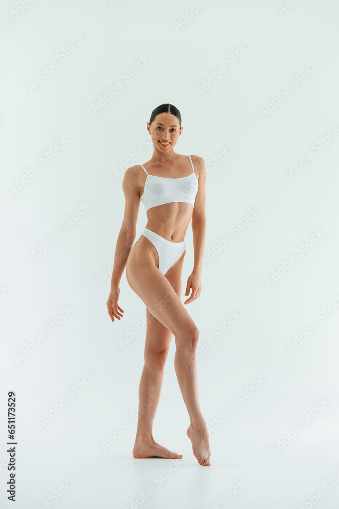 In the studio with white background. Young woman with slim body type is in fitness clothes