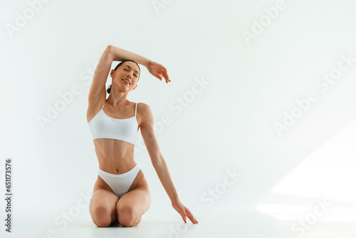 Front view, on the floor. Young woman with slim body type is in fitness clothes in the studio