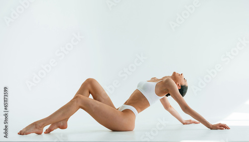 View from the side, on the floor. Young woman with slim body type is in fitness clothes in the studio