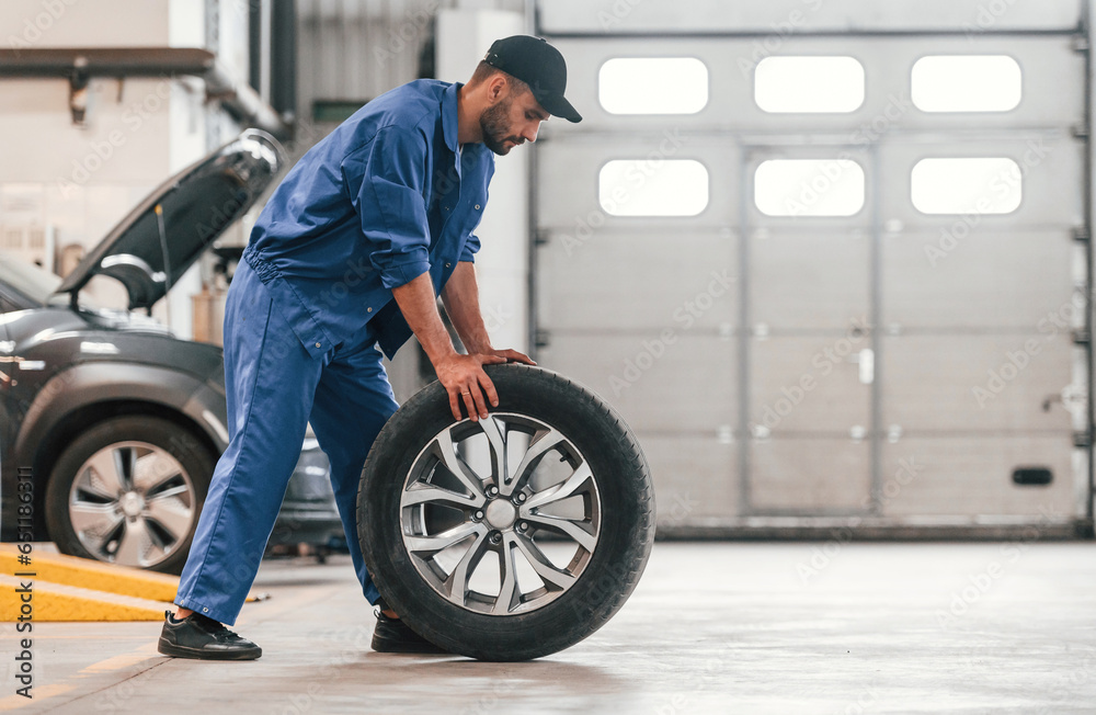 Side view. Moving the new tire. Auto mechanic working in garage. Repair service Side view. Moving the new tire. Auto mechanic working in garage. Repair service