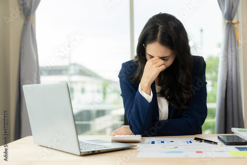 Tired young freelance worker rubbing eyes while sitting in front of laptop computer and office syndrome concept, young Asian woman tired, overworked, feeling headache, having vision problems © MrAshi