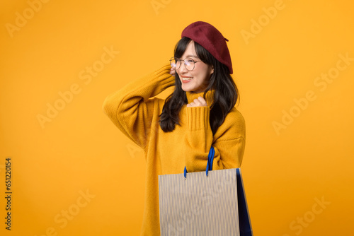 A happy young woman in a red beret and yellow sweater enjoys her shopping spree, holding a paper bag against a vibrant yellow background. photo